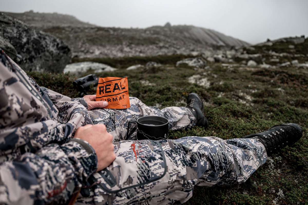 A hunter eats small refreshments and drinks from the thermos